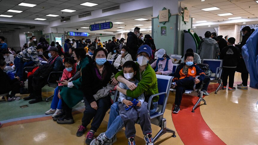 People wearing masks sit in a crowded hospital waiting room.