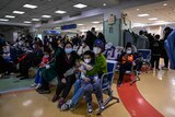 People wearing masks sit in a crowded hospital waiting room.
