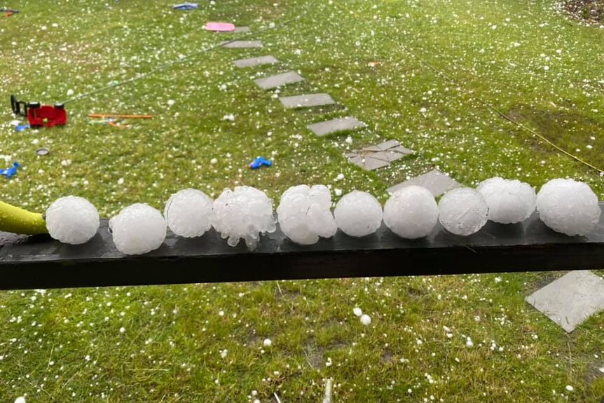 Huge hail stones lined up on a handrail at a house at Willowbank, with the backyard in view also covered in hail.