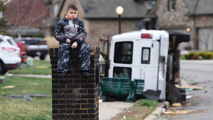 Gio Rodriguez, 8, sits outside his home as his parents clean up debris after a storm hit.