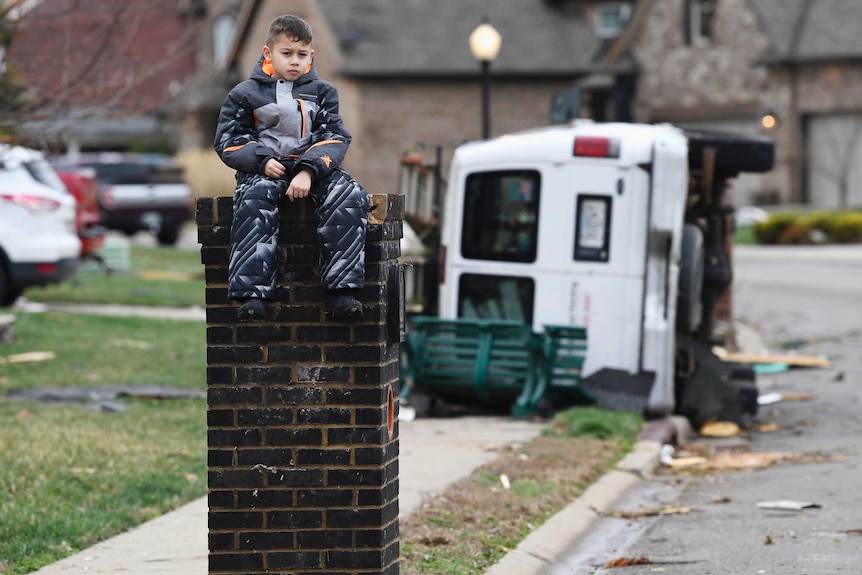 Gio Rodriguez, 8, sits outside his home as his parents clean up debris after a storm hit.