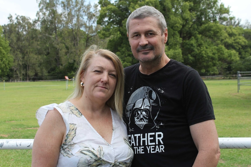 A woman in a white shirt stands next to a man in a black shirt in a park