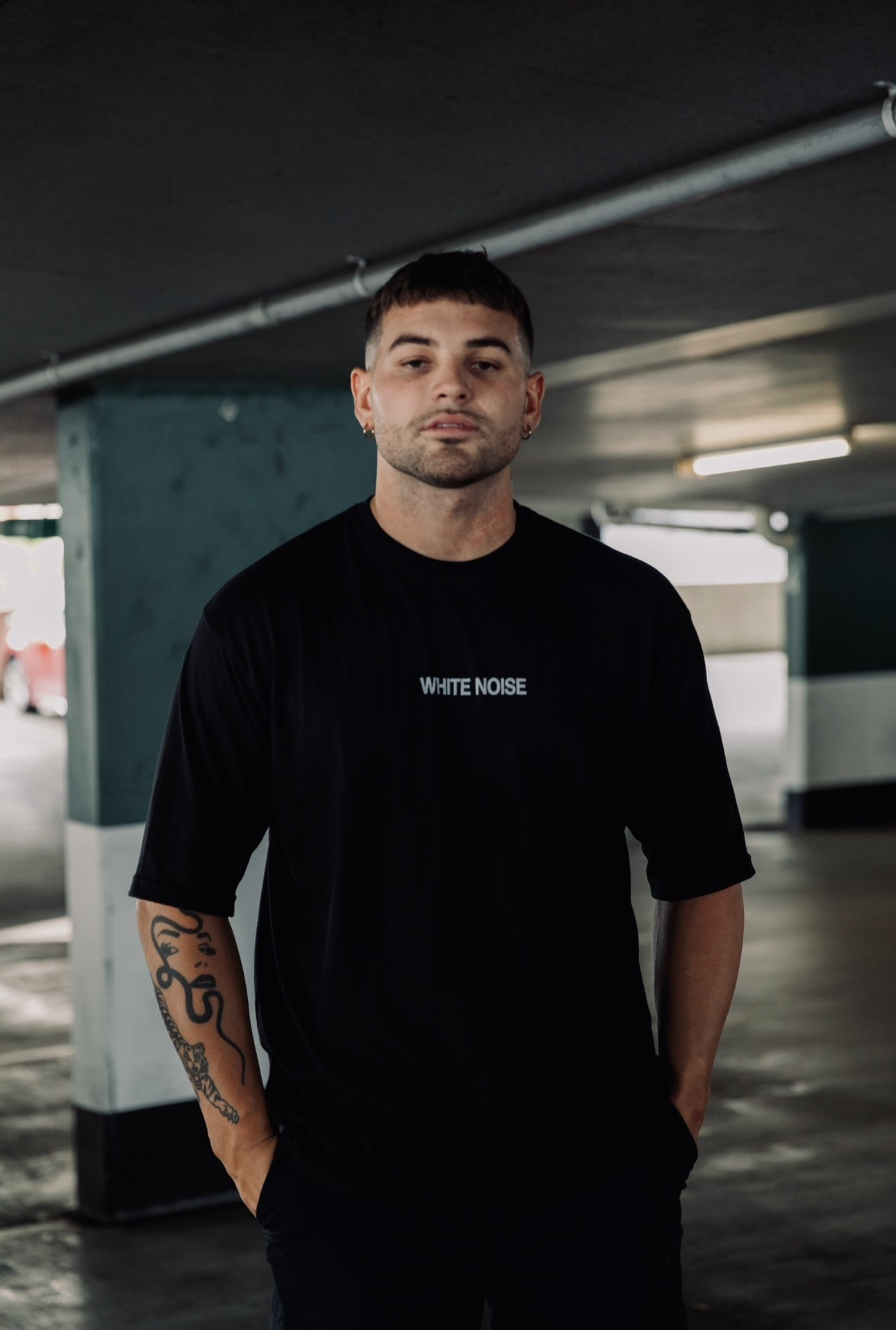 Um homem com um corte de cabelo moderno parece pensativo para a câmera em um estacionamento escuro.