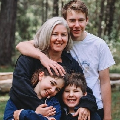 A lady hugging her three children as they all smile at the camera in a park