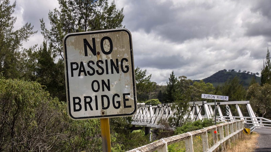 A no passing on bridge sign with a white timber bridge in the background