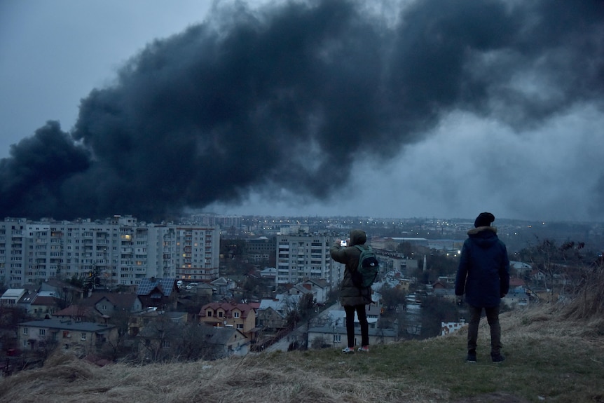 Two people watch smoke rise above building from a hill in Lviv.