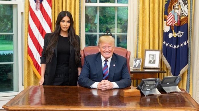 Donald Trump seated behind a table and Kim Kardashian standing beside him.