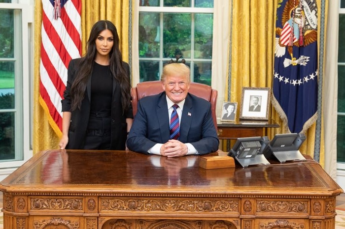 Donald Trump seated behind a table and Kim Kardashian standing next to him.