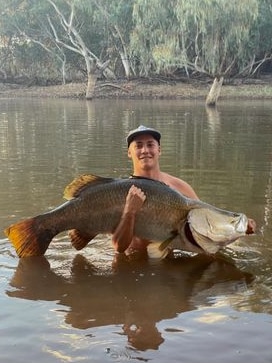 Man stands in river holding large fish