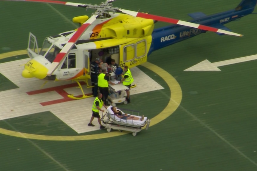 An aerial view of two passengers on stretchers being wheleed away from a helicopter.