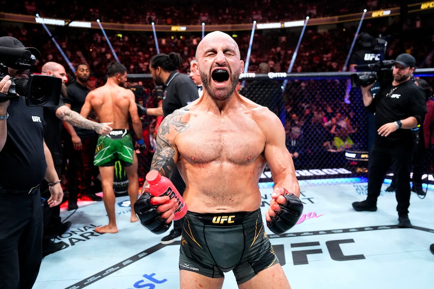 A shirtless man screams in celebration in the fighting octagon.