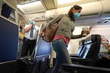 A woman in a facemask walks down the aisle of a plane.