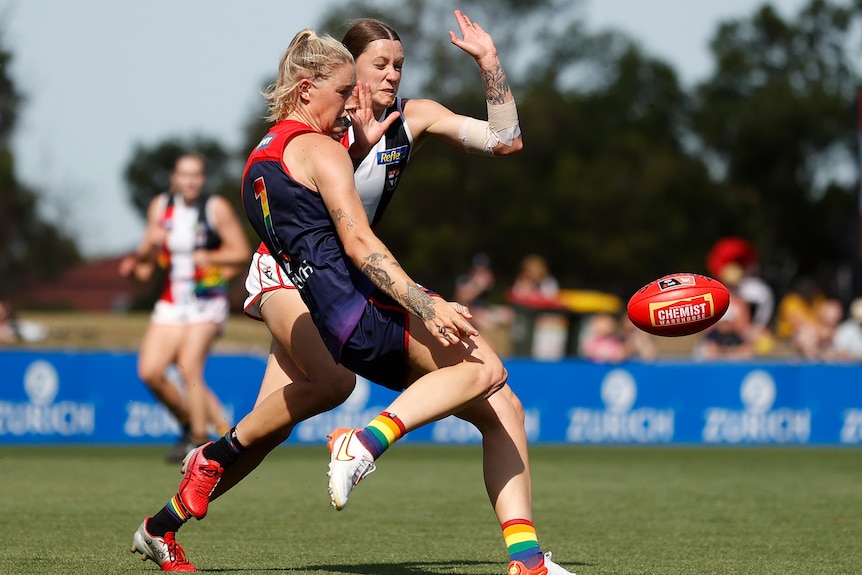 Demons AFLW player Tayla Harris kicking the ball during a match while being defended by Saints' Bianca Jakobsson