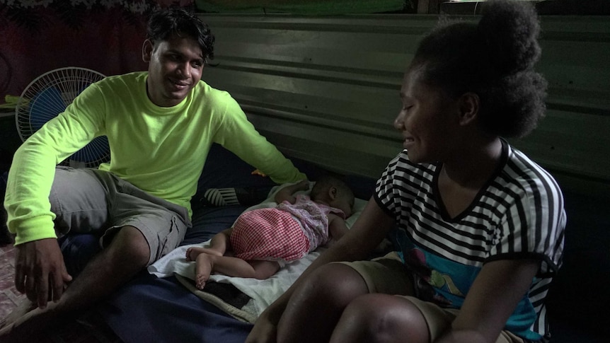 A man and woman sit on the floor on either side of a baby.