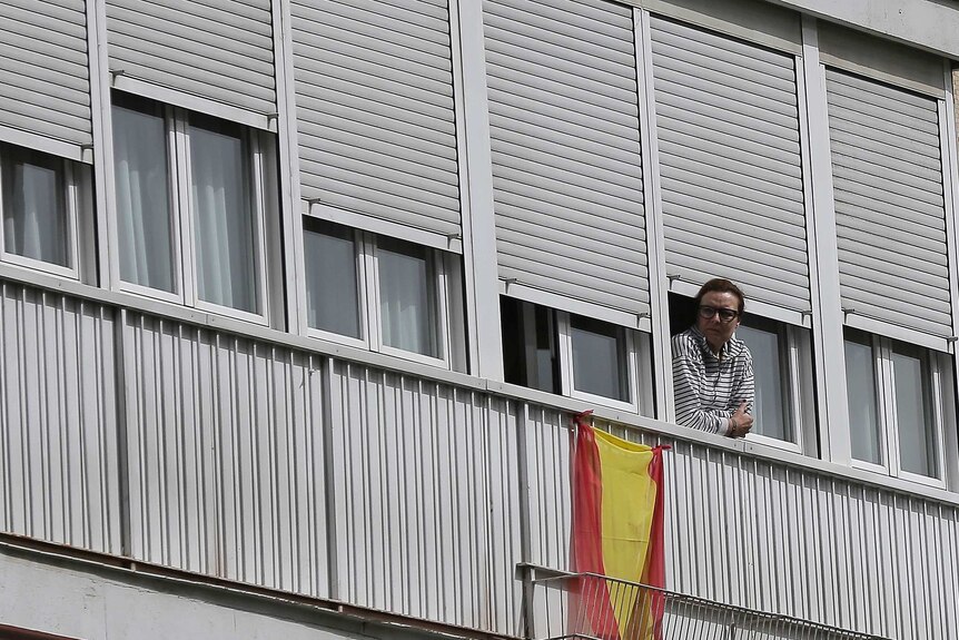 A woman looks out from a balcony next to a Spanish flag in Madrid, Spain.
