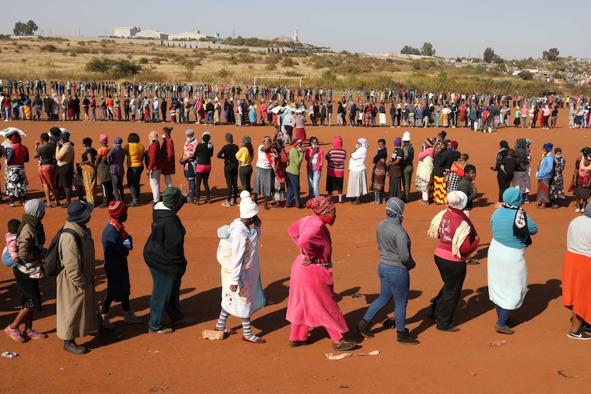 A long line of people in a dirt field in South Africa