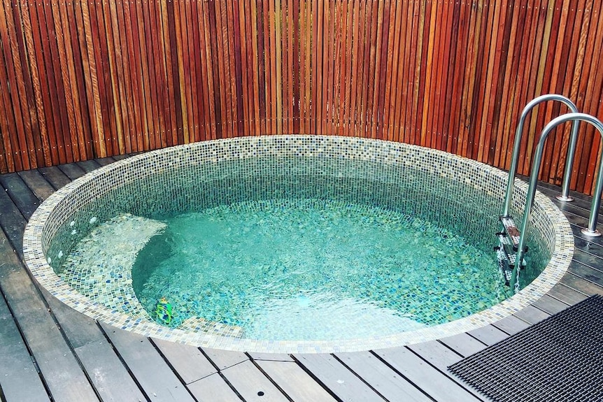 Concrete plunge pool in backyard out west surrounded by rusted steel fence and wooden deck and stairs.