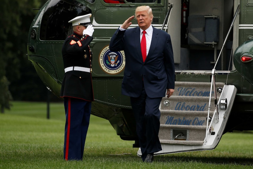 Trump salutes a marine as he leaves the presidential helicopter.
