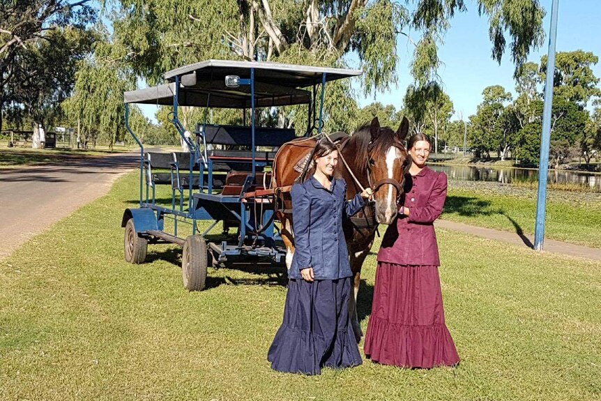 Two women dressed in period costume in front of a horse and carriage