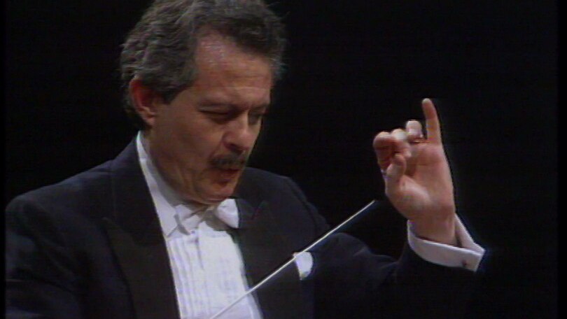 Conductor Jorge Mester in dinner suit with white bow-tie with left hand raised and baton appearing from the right