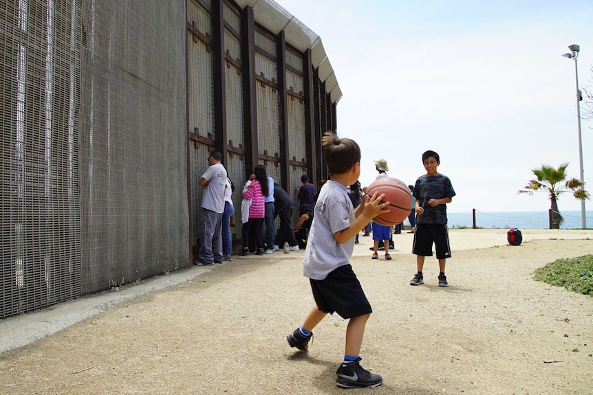 Children play with a ball on the US side of the Mexico border, while their parents chat to relatives through the fence.