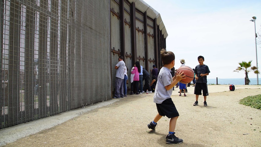 Children play with a ball on the US side of the Mexico border, while their parents chat to relatives through the fence.