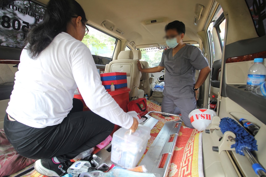 A man and woman crouching in the back of a van filled with medical equipment