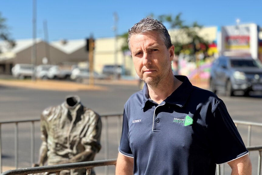 man with blue polo posing in front of defaced statue