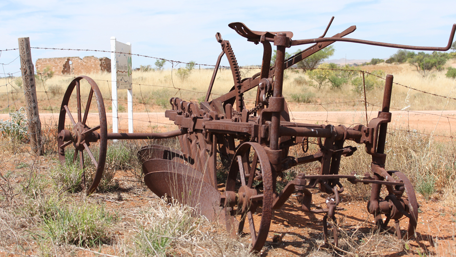 A rusted plough from the turn of the century left abandoned in a patch of grass by the roadside