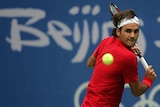 A headband-wearing Olympics men's tennis player focuses on ball as he prepares to hit a backhand.