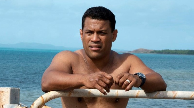 Shirtless man leans on fence near ocean