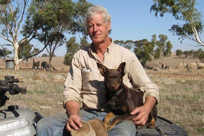 A man sits on a quad bike on a rural property with a kelpie dog in his lap.