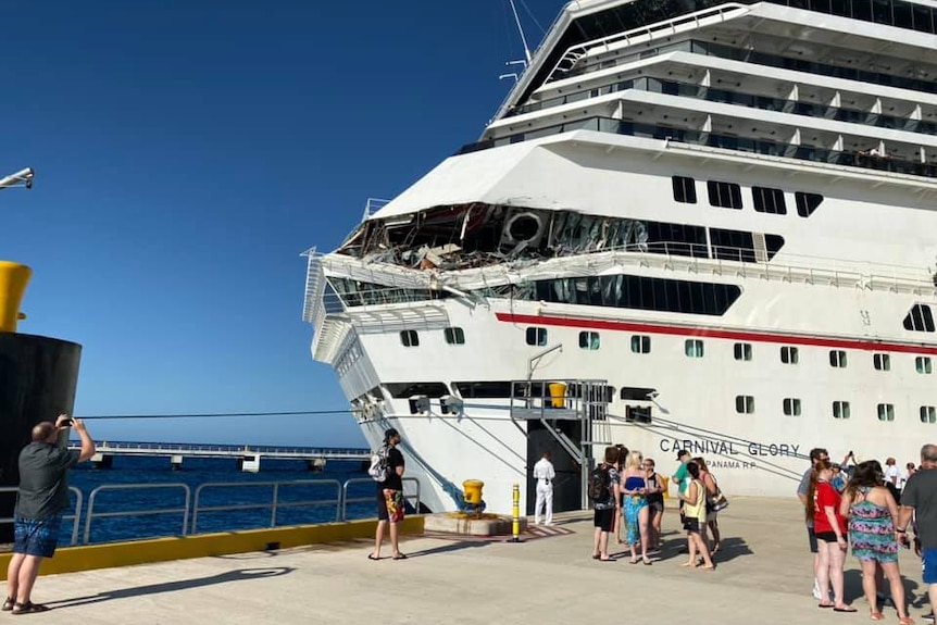 the carnival glory is docked with damage to its decks with people standing in front of it