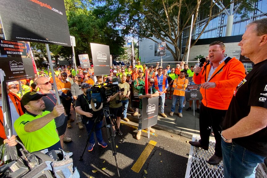 a group of protesters gather at a stage in high vis