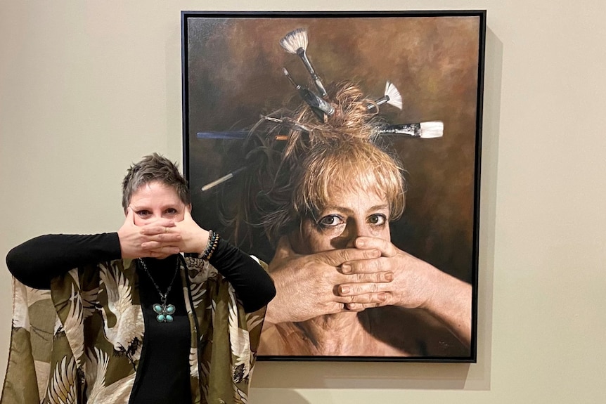 Jaq holds her hands over her mouth, copying her pose in the painting behind her.