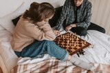 Man and woman playing chess on a bed, in a story about practical ways to help your mental health during COVID lockdown.