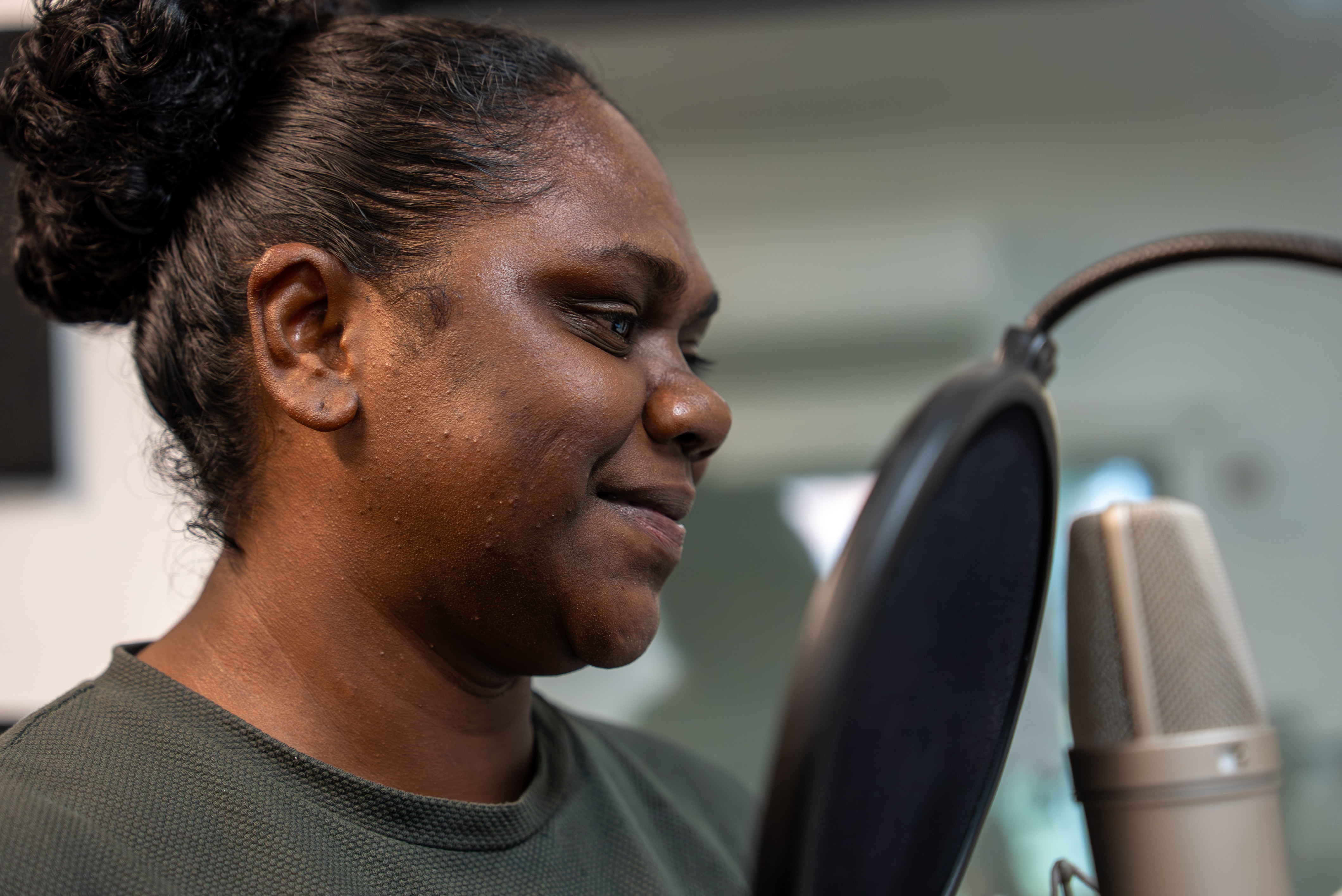 Ms Mununggurr is smiling in front of a microphone. She has balck curly hair tied up and wearing a t-shirt.