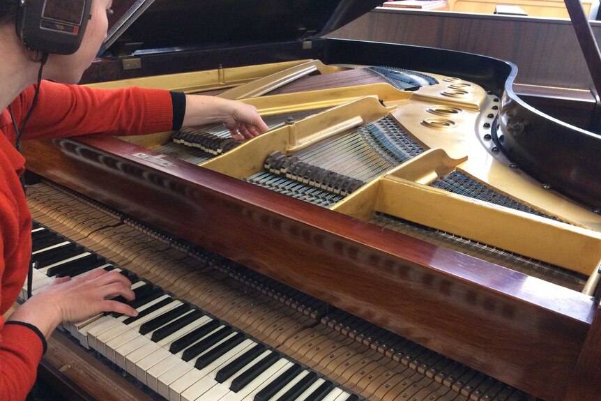 A woman in headphones leans over a open piano to make some adjustments.