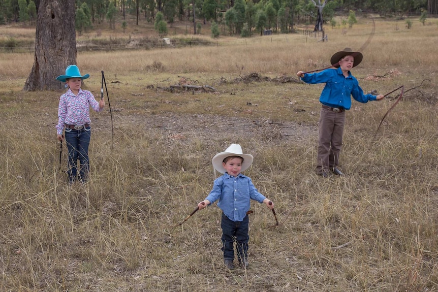 Three children in a paddock cracking whips