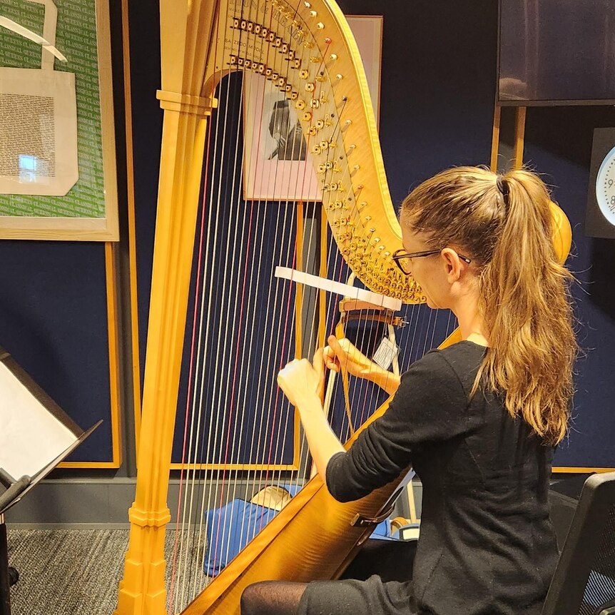 Genevieve Lang plays the harp in the studio with a piece of paper threaded through the strings