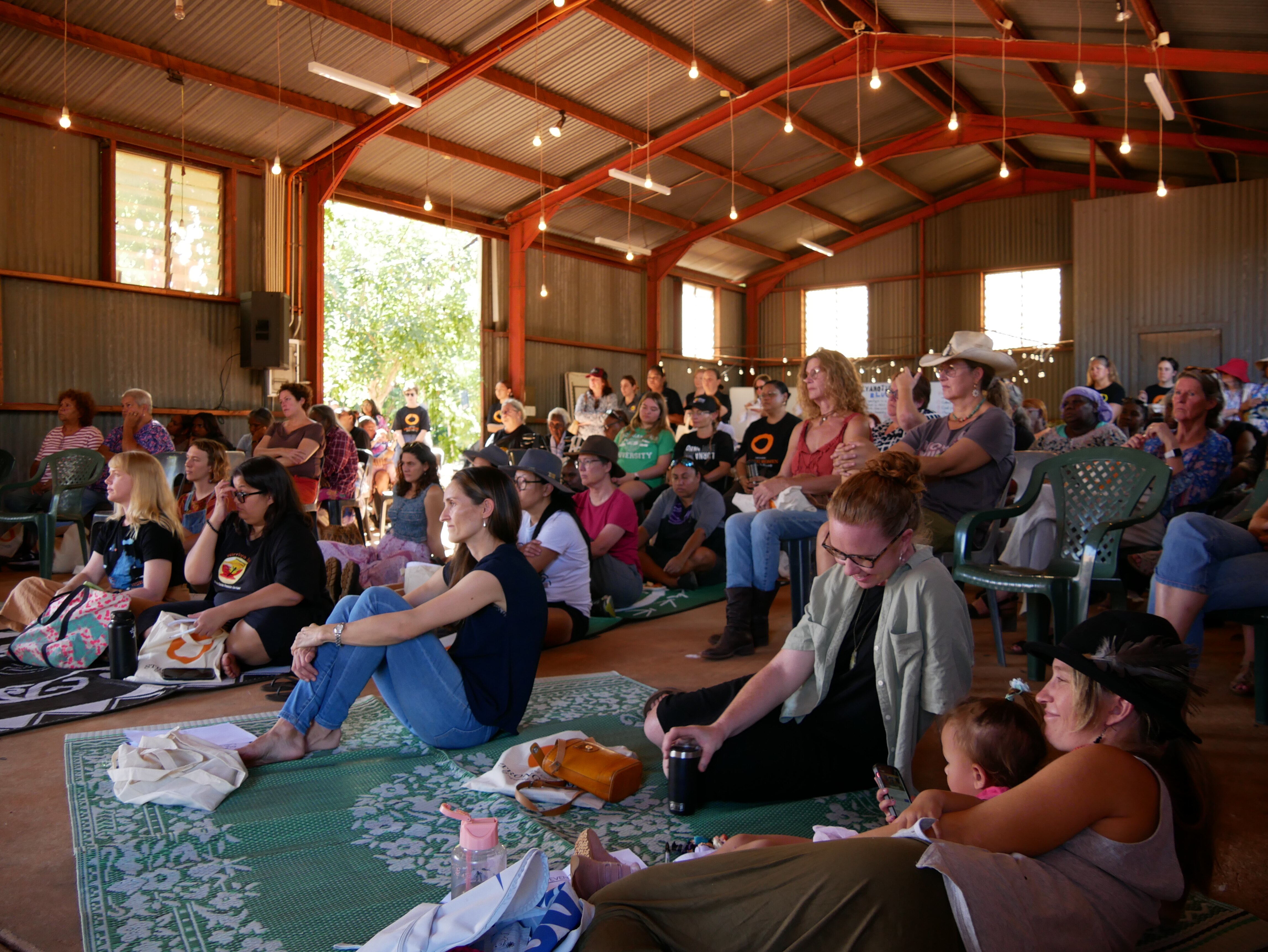 Women sit on the floor and in chairs as they listen to a speaker