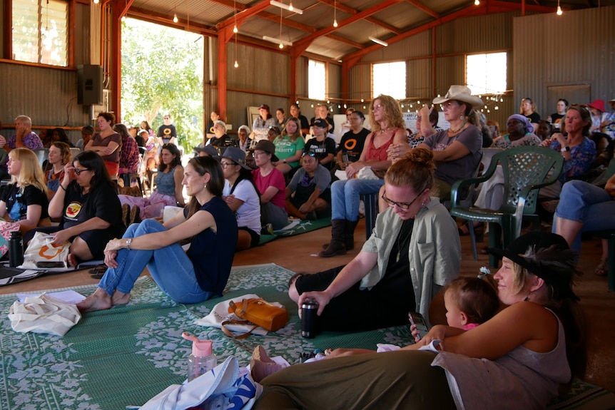 Women sit on the floor and in chairs as they listen to a speaker