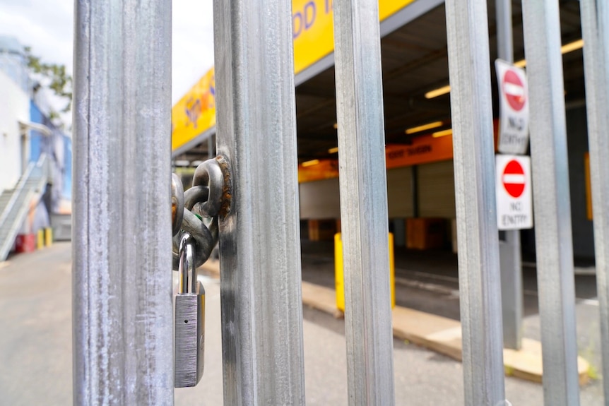 A locked gate with a padlock, with a drive-thru bottle shop in the background