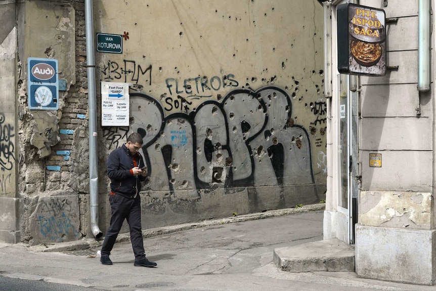 A man walks past a bullet hole-riddled wall in Sarajevo.