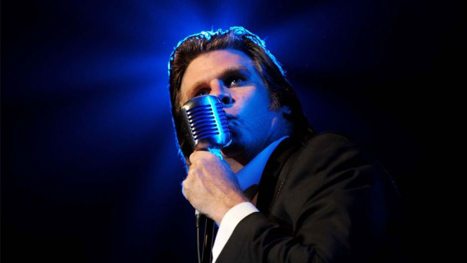 A man in a black suit holds a microphone.