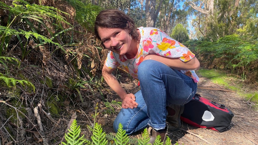Smiling woman crouches down on bush track.
