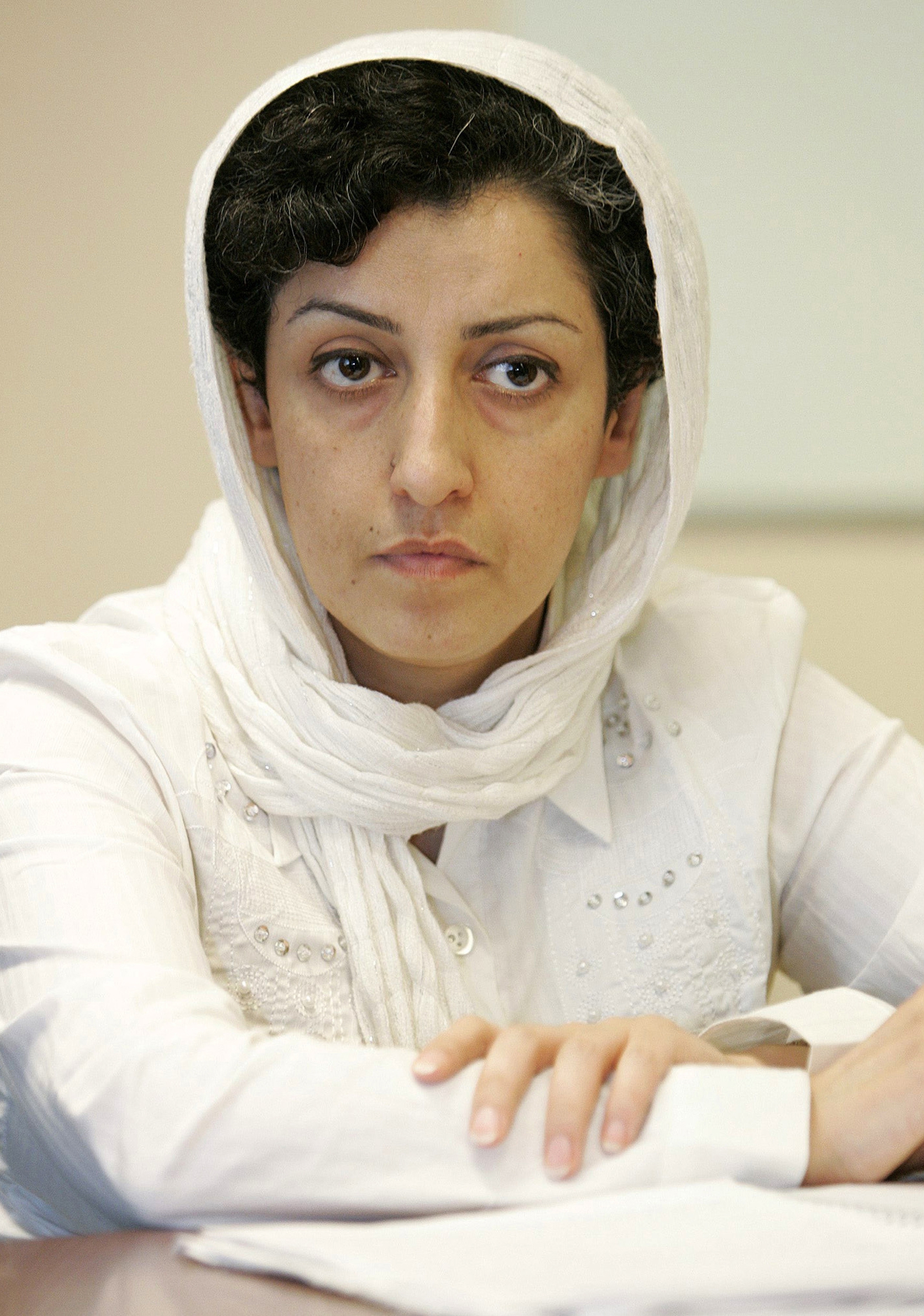 Woman in white, including white hijab, looks sternly at the camera. 