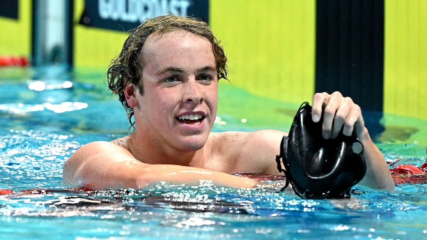 Sam Short holds his swimming cap in his hand while floating in the pool after finishing a race