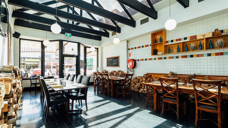 The interior of a bistro dining room with tables and chairs looking out onto the street.