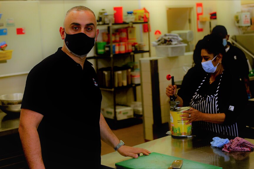 A man wearing a black mask stands in community kitchen.